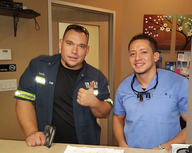 Two men posing together in dental office, one wearing police uniform, both smiling at camera.