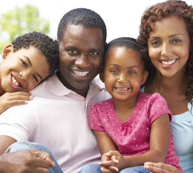 Happy family of four smiling together outdoors in casual clothing.